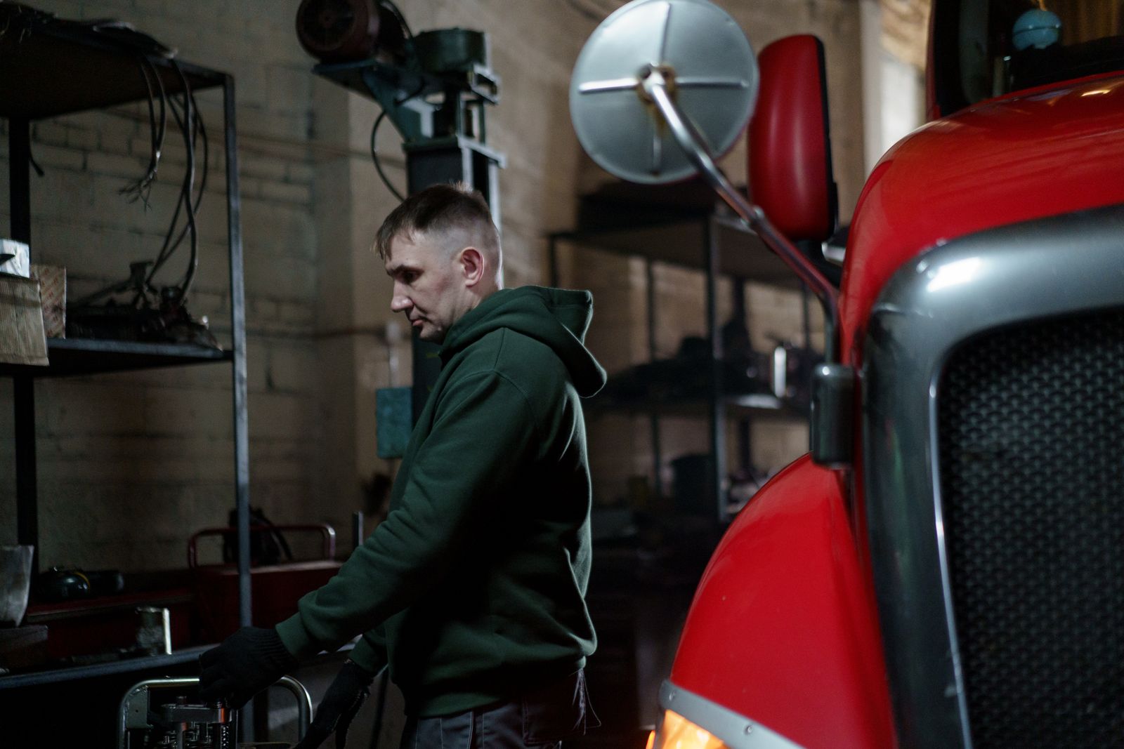 A mechanic at his tools beside a red semi truck in a repair workshop